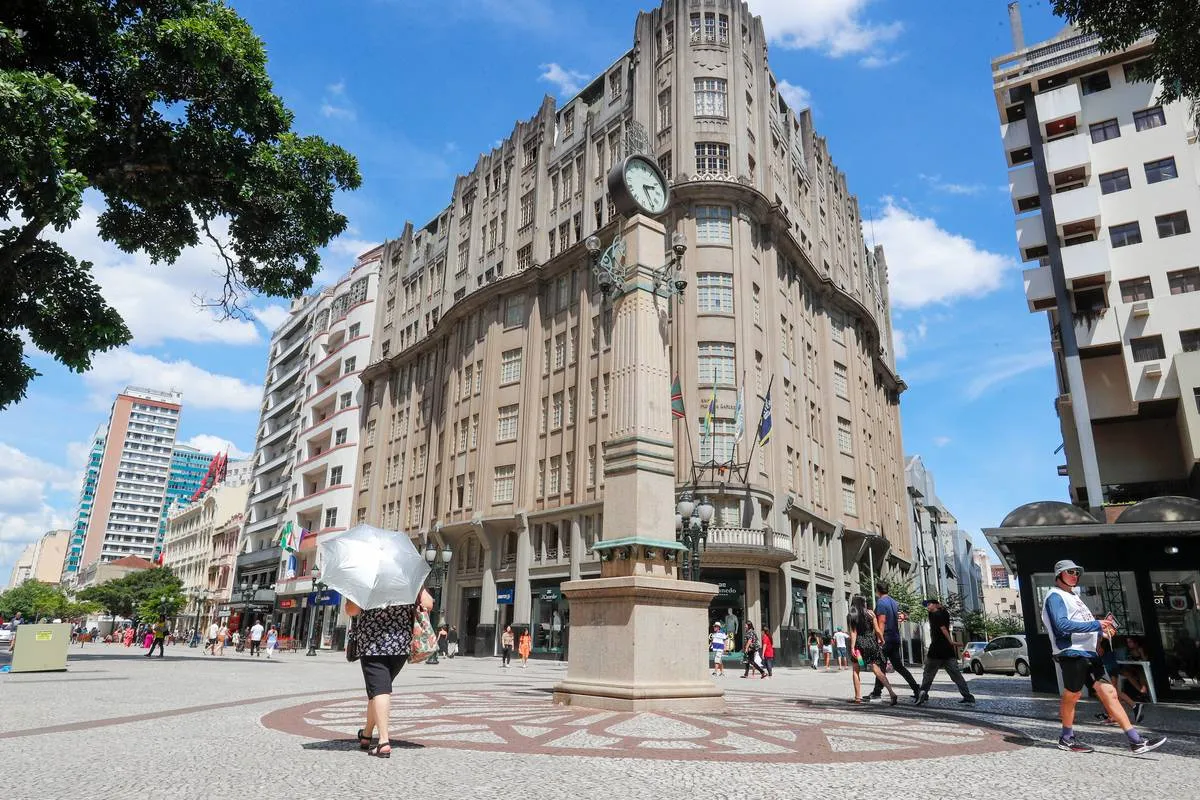 Imagem mostra um prédio em Curitiba, com céu azul e um grande relógio ao centro.