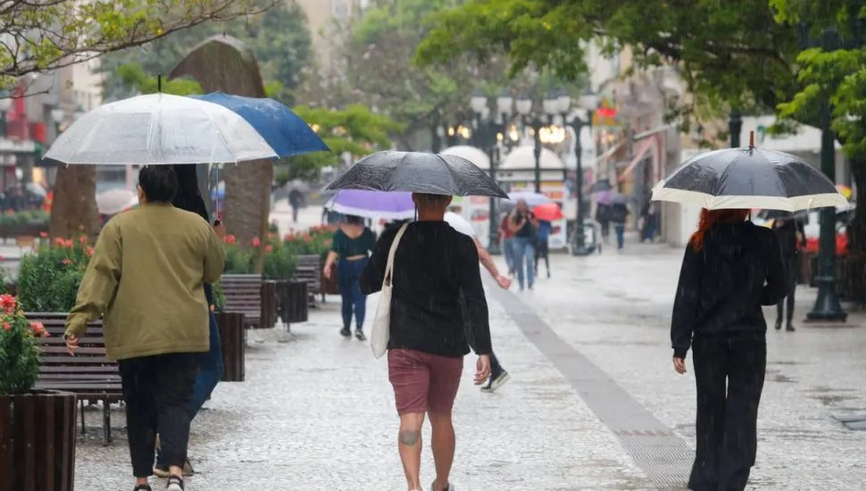 Imagem mostra pessoas andando em meio a uma forte chuva na Rua XV, em Curitiba.