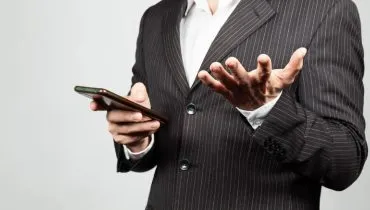 Imagem mostra um homem de terno usando um celular.