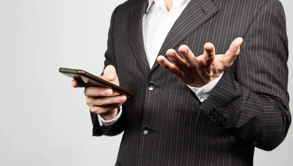 Imagem mostra um homem de terno usando um celular.