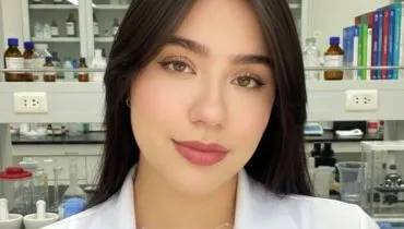 Imagem mostra uma jovem com cabelos pretos e blusa branca em um laboratório.