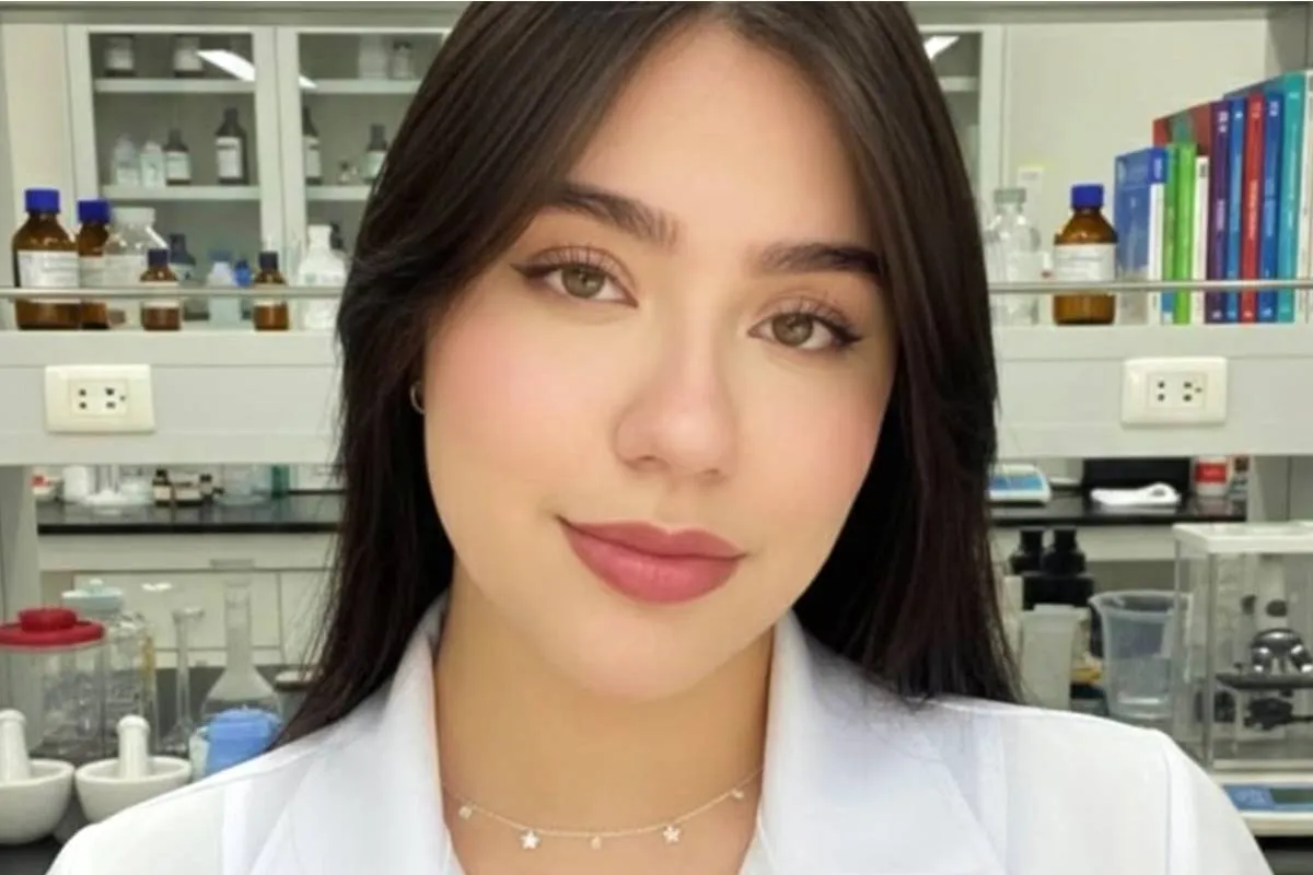 Imagem mostra uma jovem com cabelos pretos e blusa branca em um laboratório.