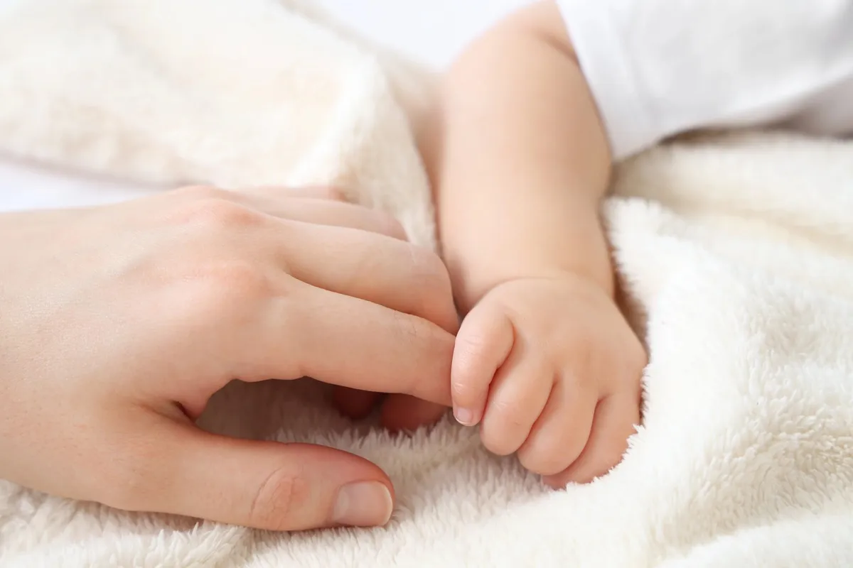 Imagem mostra mãozinha de bebê e mão de pessoa adulta