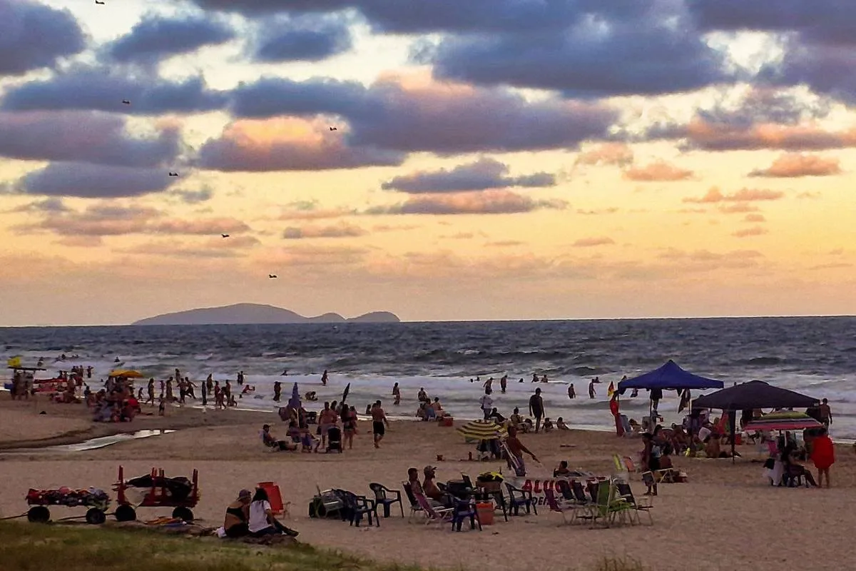 Imagem mostra veranistas no litoral do Paraná durante o por do sol