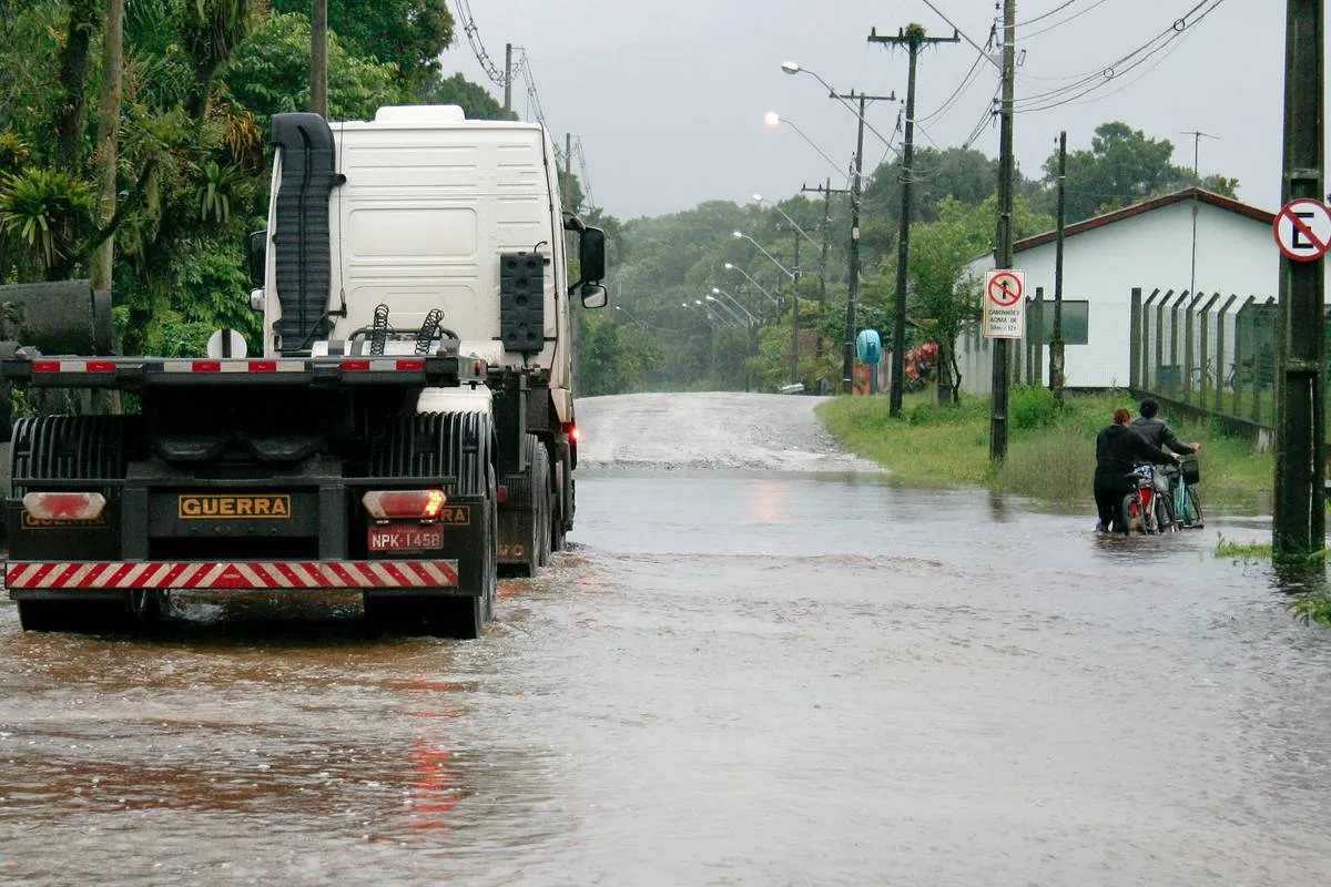 Imagem mostra uma rua apagada e um caminhão atravessando a rua com água alta.
