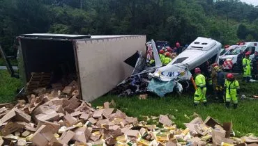 Imagem mostra um cenário de um grave acidente. Com uma van destruída e um caminhão com carga espalhada.