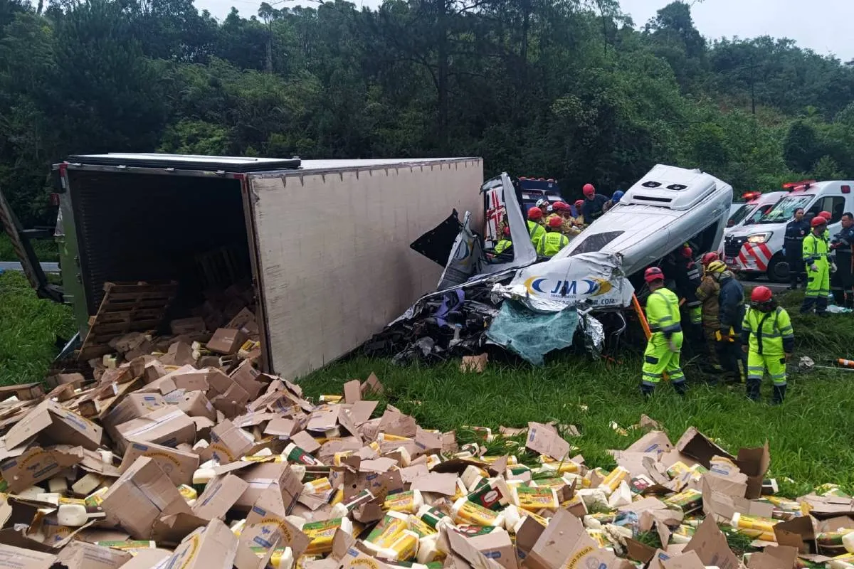 Imagem mostra um cenário de um grave acidente. Com uma van destruída e um caminhão com carga espalhada.