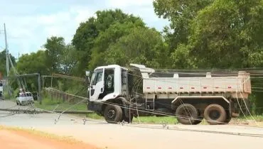 Imagem mostra um caminhão com fios de luz enroscados em uma estrada de chão em Curitiba.