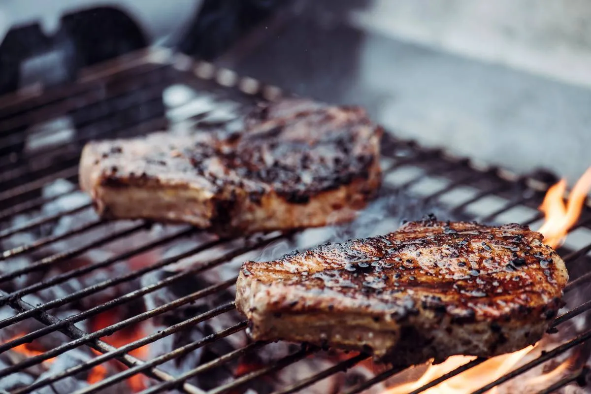Imagem mostre uma carne sendo grelhada numa churrasqueira