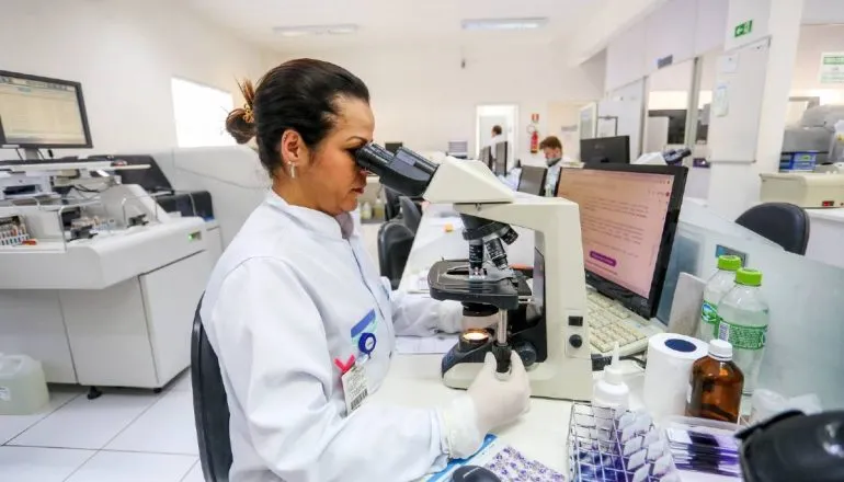 Imagem mostra uma pessoa olhando em um microscópio em um laboratório.