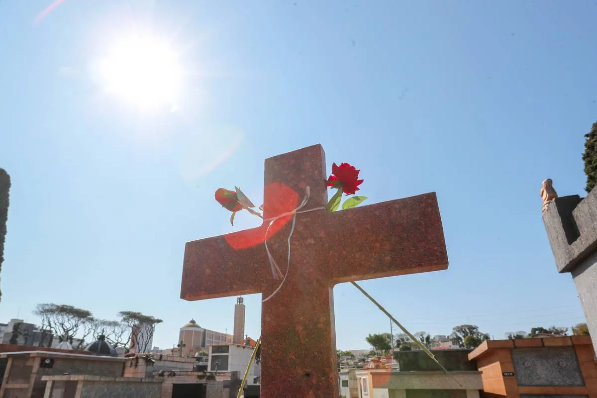 Imagem mostra um detalhe de um cemitério em Curitiba, com uma cruz e túmulos.