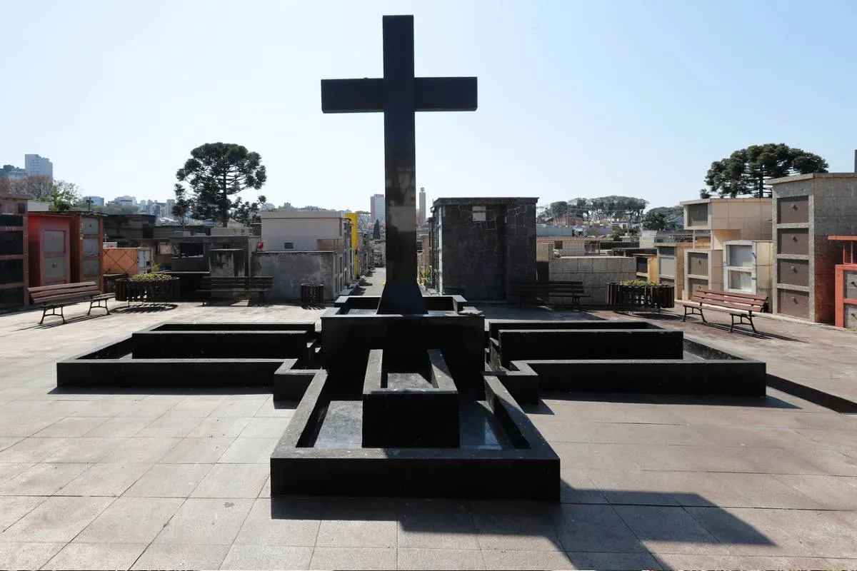 Imagem mostra um detalhe de um cemitério em Curitiba, com uma cruz e túmulos.