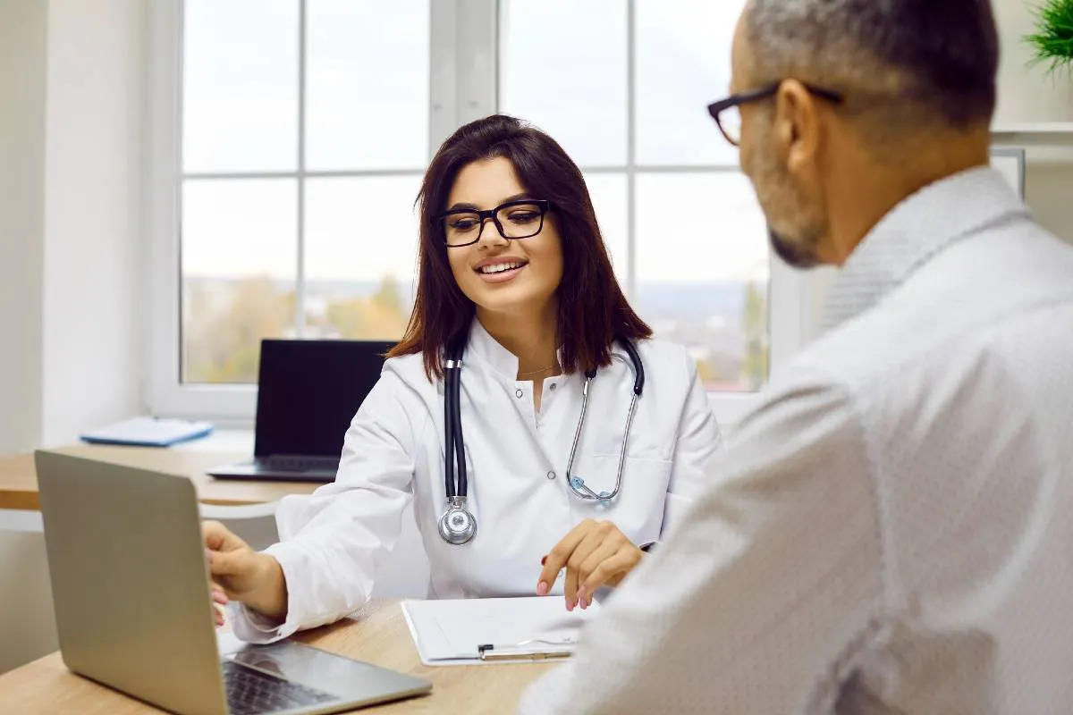 Imagem mostra uma médica conversando com um paciente em uma consulta.