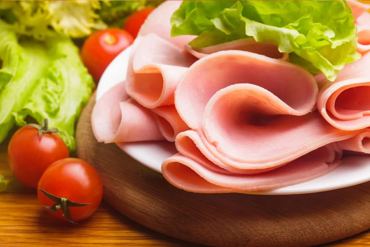Imagem mostra um presunto em uma tábua de madeira com tomates.