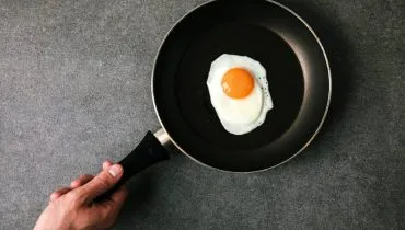 Imagem mostra um ovo frito em uma frigideira preta.