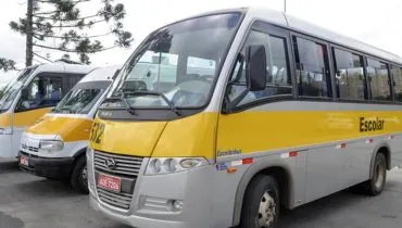 Imagem mostra vans escolares estacionadas ao lado de um microonibus.
