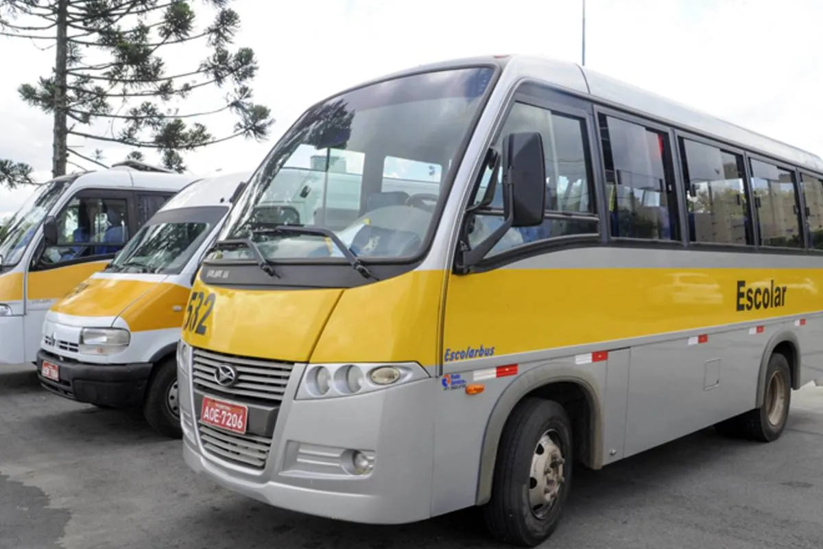 Imagem mostra vans escolares estacionadas ao lado de um microonibus.