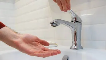 Imagem mostra uma pessoa tentando lavar a mão em uma torneira sem água.