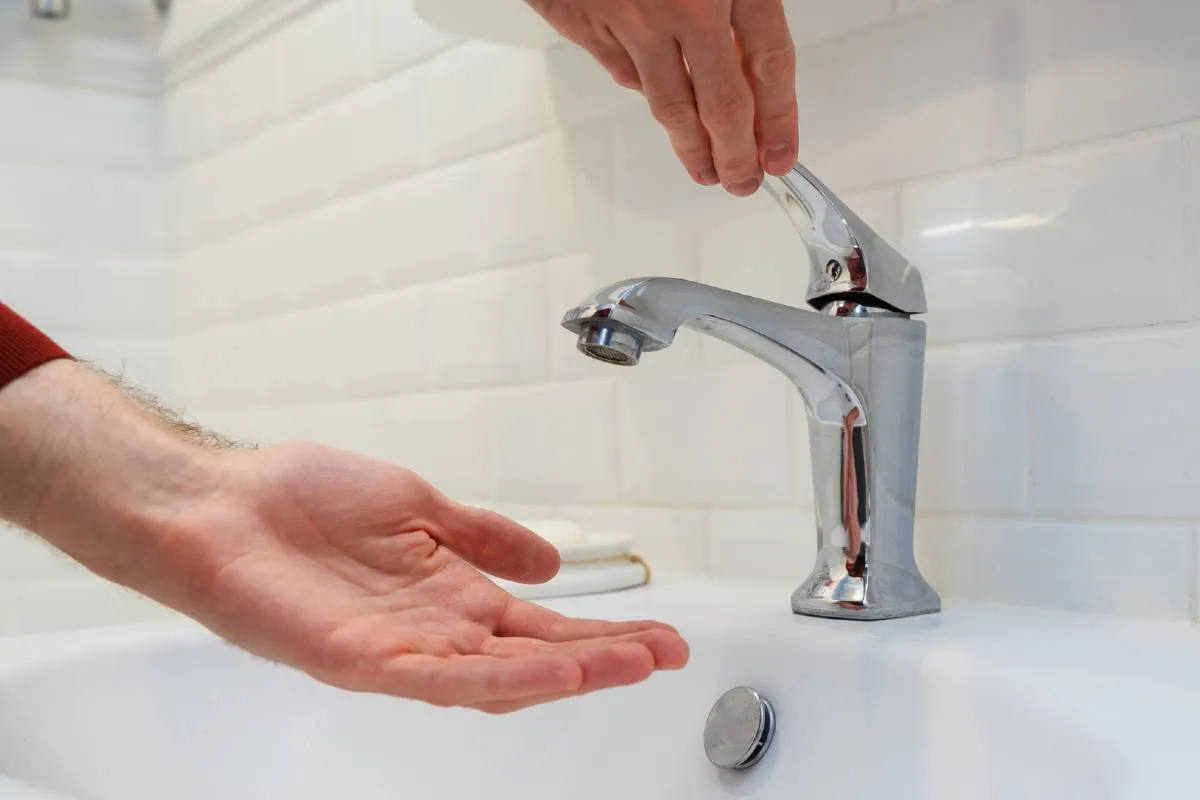 Imagem mostra uma pessoa tentando lavar a mão em uma torneira sem água.