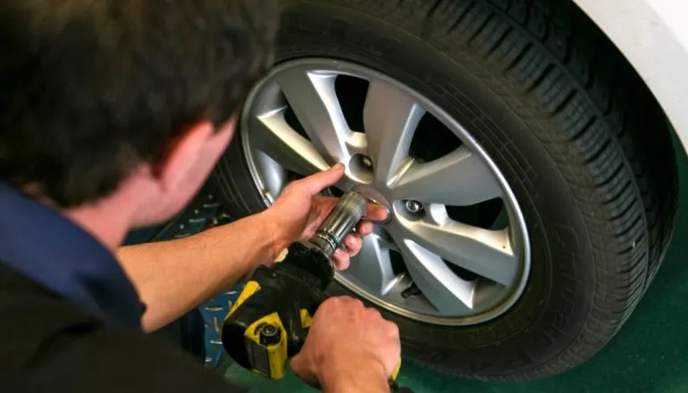 Imagem mostra um mecânico trocando o pneu de um carro.