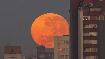 Imagem mostra a Lua de Sangue surgindo por trás de prédios em Curitiba.