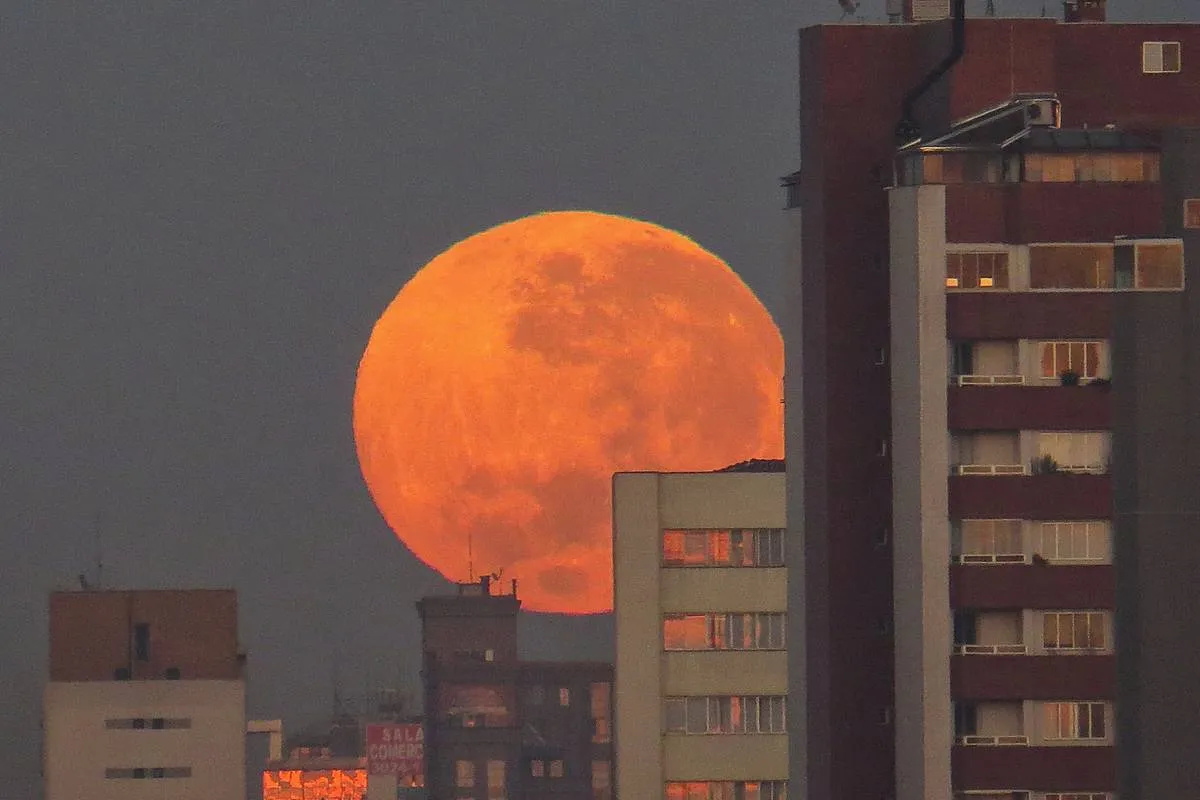 Imagem mostra a Lua de Sangue surgindo por trás de prédios em Curitiba.