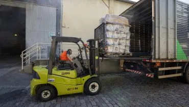 Imagem mostra uma empilhadeira verde carregando mantimentos em um caminhão.