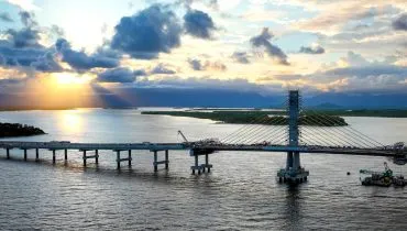 Imagem mostra a obra da Ponte de Guaratuba com um belo por do sol ao fundo.