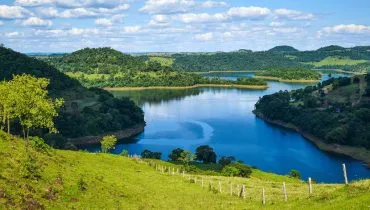 Imagem mostra um trecho com um lago e floresta e um dia de sol.