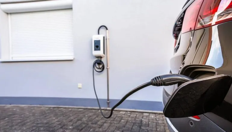 Imagem mostra um wallbox e um carro preto sendo carregado.