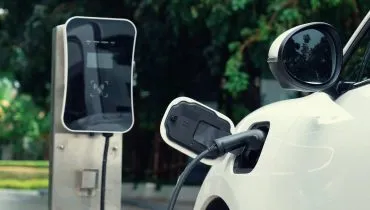 Imagem mostra um carro elétrico branco sendo carregado.