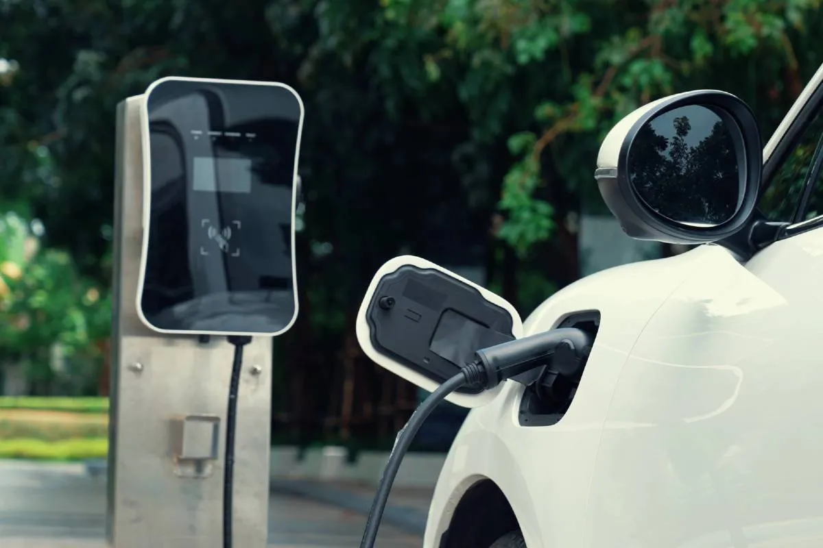 Imagem mostra um carro elétrico branco sendo carregado.