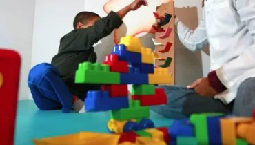 Imagem mostra uma criança recebendo atendimento e brincando ao lado de uma profissional que veste jaleco branco.