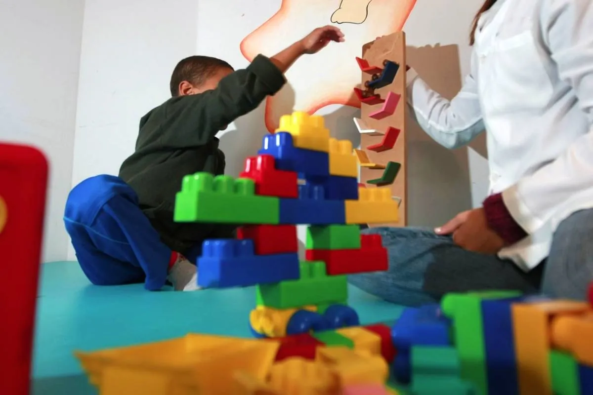 Imagem mostra uma criança recebendo atendimento e brincando ao lado de uma profissional que veste jaleco branco.