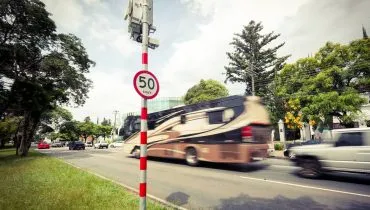 Imagem mostra um radar com uma placa de 50 km/h com um ônibus dourado passando ao fundo.