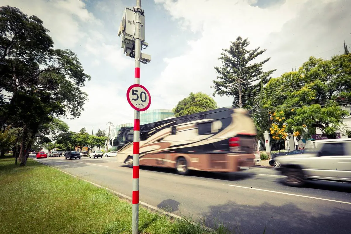Imagem mostra um radar com uma placa de 50 km/h com um ônibus dourado passando ao fundo.