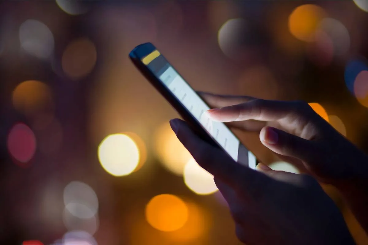 Imagem mostra uma pessoa usando um celular durante a noite.