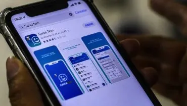Imagem mostra uma pessoa segurando um celular aberto na página de instalação ao app Caixa Tem.