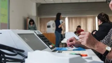 Imagem mostra uma mesária voluntária na frente de uma urna eletrônica no Paraná.