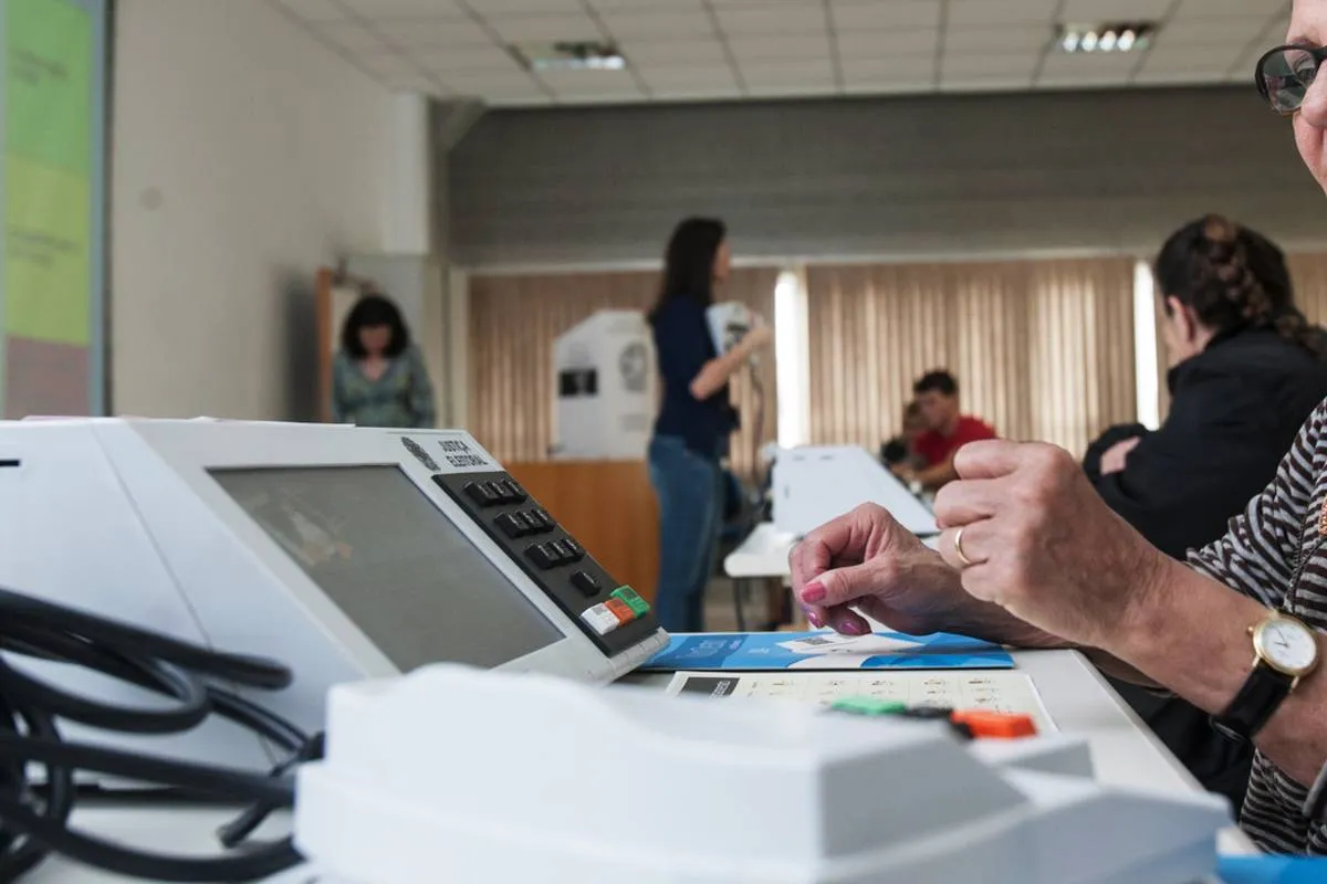 Imagem mostra uma mesária voluntária na frente de uma urna eletrônica no Paraná.