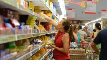 Imagem mostra uma mulher escolheiro produtos em uma prateleira de supermercado.