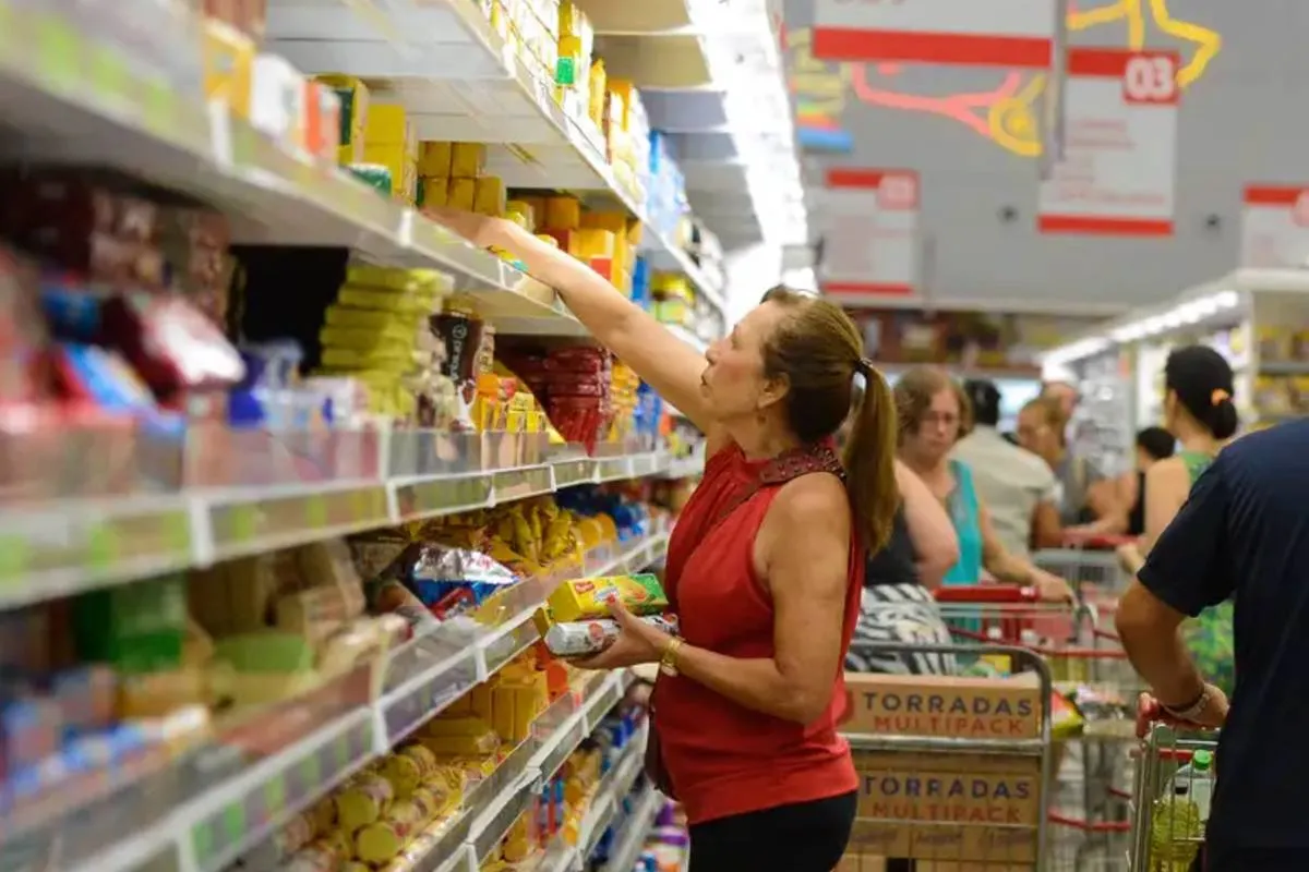 Imagem mostra uma mulher escolheiro produtos em uma prateleira de supermercado.