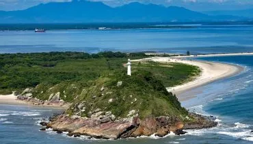 Imagem aérea mostra o farol da Ilha do Mel, com Paranaguá ao fundo