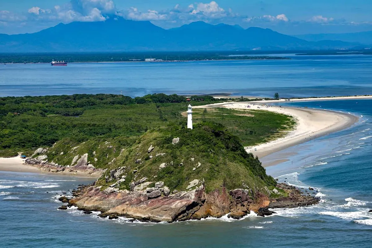 Imagem aérea mostra o farol da Ilha do Mel, com Paranaguá ao fundo