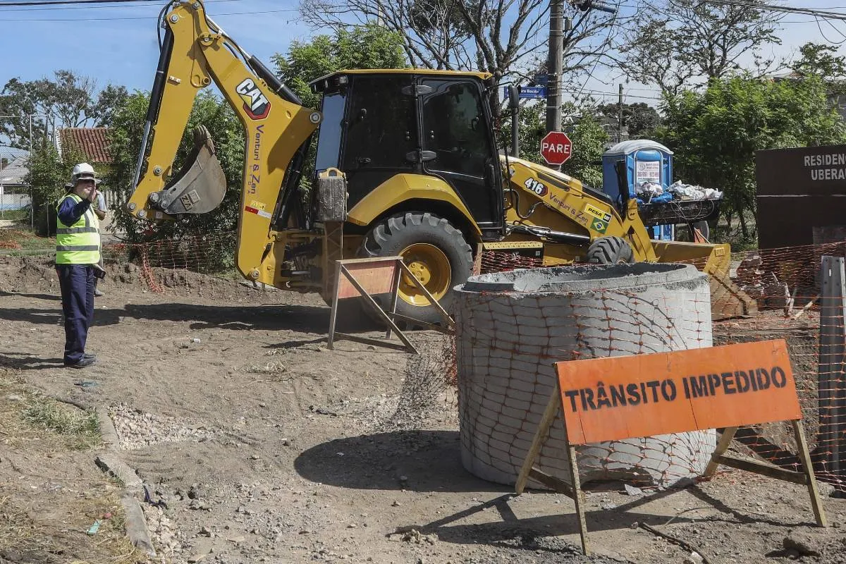 Imagem mostra uma obra no meio de uma rua de Curitiba. Há uma retroescavadeira e uma placa de 'trânsito impedido"