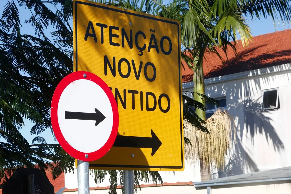 Imagem mostra duas placas de trânsito. Uma vermelha e branca indica um novo sentido. A outra, toda amarela com letras pretas diz: Atenção, novo sentido.