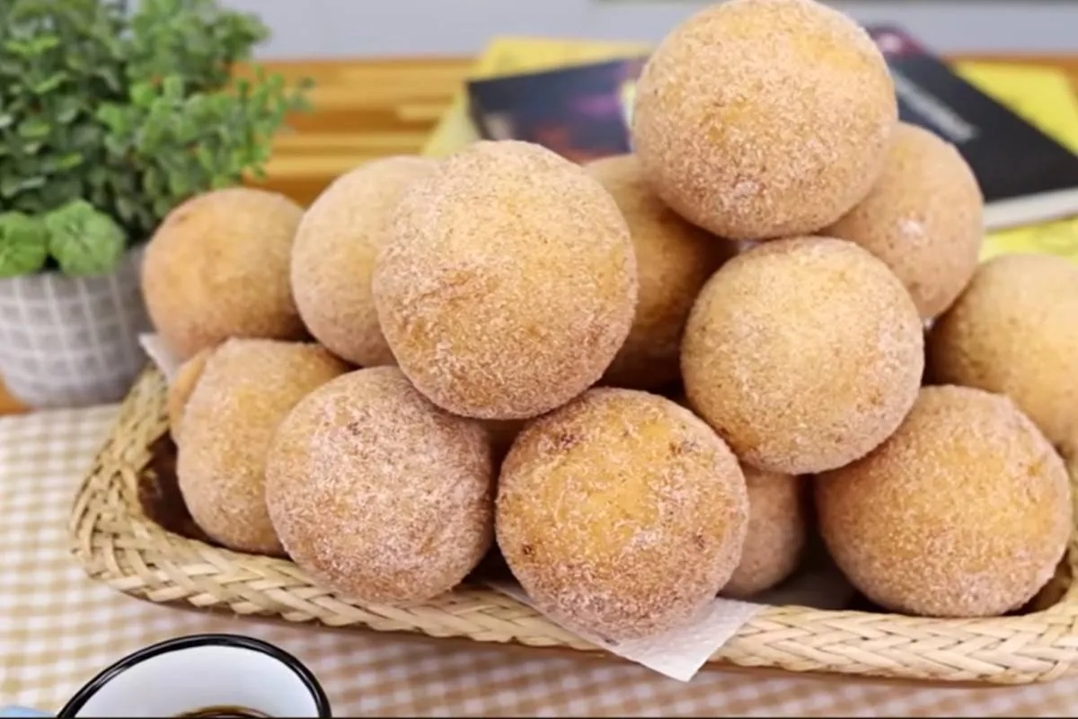 Imagem mostra bolinhos de chuva recém fritos, com açúcar polvilhado e uma xícara de café.
