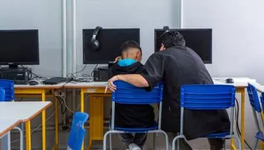 Imagem mostra um aluno com o pai lendo uma apostila na frente de um computador.