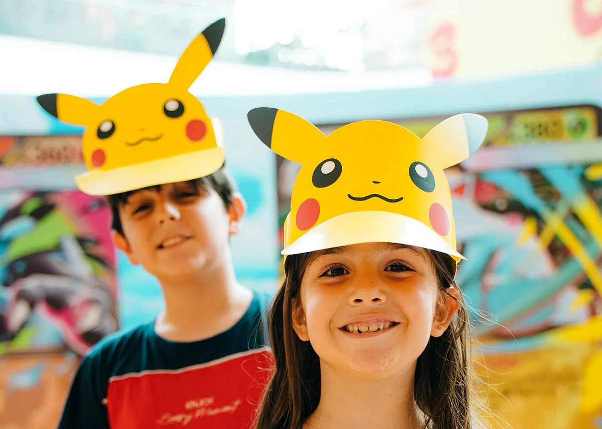 imagem mostra duas crianças, um menino e uma menina, com chapéus de pikachu