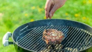 Imagem mostra uma pessoa salgando uma carne que está na grelha com sal grosso.